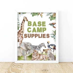 May include: A framed print with watercolor illustrations of safari animals, including a giraffe, elephant, zebra, lion, and cheetah. The text "BASE CAMP SUPPLIES" is in green and brown stitched letters, surrounded by tropical foliage.