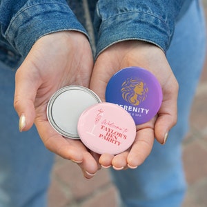 May include: Three round buttons with different designs. The first button is pink with a champagne glass and the text "Welcome to Taylor's Hen Party". The second button is white with a silver rim. The third button is purple with a woman's face and the text "Serenity Salon & Spa".