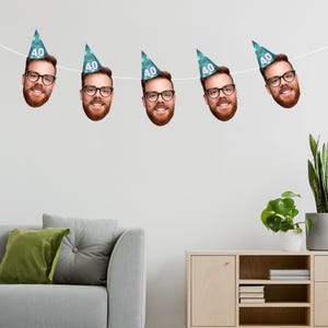 Personalised birthday bunting featuring multiple cutouts of a smiling man’s face wearing blue party hats with the number 40 printed on them. The bunting is strung across a modern living space, creating a fun and customised decoration for a 40th birthday celebration. A unique and playful party accessory perfect for adding a personal touch to milestone events.