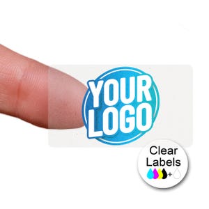 May include: A clear rectangular label with the text "YOUR LOGO" in white within a blue circle. A finger touches the label. A smaller white circle with the text "Clear Labels" and colour drops is in the lower right.