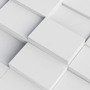 Neatly stacked piles of blank white business cards arranged in a grid pattern, displaying a clean and uniform appearance with a textured finish on a white surface.