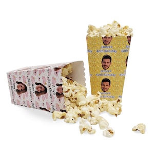 May include: Two popcorn boxes with personalised designs. One box is pink with a woman's face and the text "Amy's Baby Shower". The other box is yellow with a man's face and the text "James's 40th Birthday".