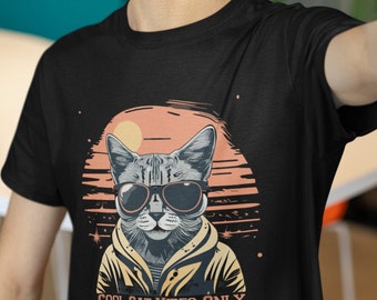May include: Black t-shirt featuring a graphic of a cat wearing sunglasses and a jacket. The cat is in front of a sunset with the text "COOL CAT VIBES ONLY" below.