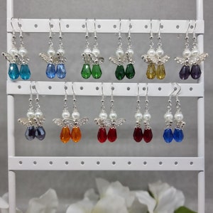 May include: A display of 12 pairs of angel wing earrings with crystal drops in various colours, including blue, green, red, orange, and purple. The earrings are displayed on a white earring stand.