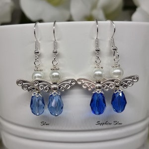 May include: A pair of silver angel wing earrings with a pearl bead and a blue crystal drop. The earrings are shown in two colours: blue and sapphire blue.