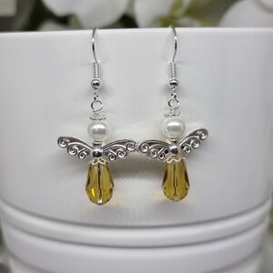 May include: A pair of silver angel dangle earrings with a white pearl and a teardrop-shaped amber crystal.