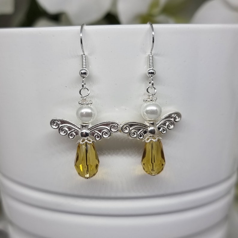 May include: A pair of silver angel dangle earrings with a white pearl and a teardrop-shaped amber crystal.