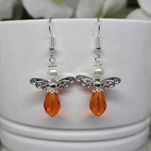 May include: Silver angel wing earrings with a white pearl and an orange crystal drop.