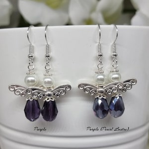 May include: A pair of silver angel dangle earrings with a white pearl and a purple crystal drop. The earrings on the right have a pearlescent purple crystal drop.