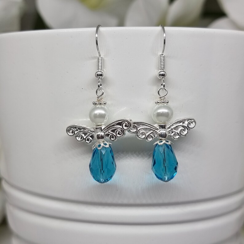 May include: Silver angel dangle earrings with a white pearl and a blue crystal drop.