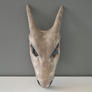 May include: A brown, textured, animal mask with large ears and black eye holes. The mask is made of a material that looks like leather or papier-mâché.