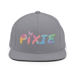 Puede incluir: Una gorra de béisbol gris de visera plana con la palabra "PIXIE" bordada en arcoíris en la parte delantera.