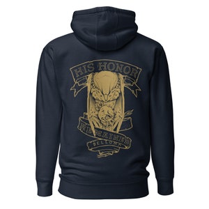 Puede incluir: Sudadera con capucha azul marino con un gráfico dorado en la espalda. El diseño presenta una criatura aviar con alas extendidas, una figura central y las palabras "HIS HONOR REMAINED BELLONA".