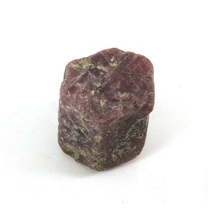 May include: A rough, dark red ruby crystal with a hexagonal shape. The crystal has a natural, unpolished finish.
