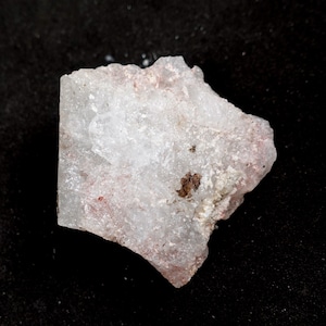 Può includere: Una roccia ruvida, bianca e rosa con alcune macchie marroni. La roccia ha un aspetto leggermente traslucido.