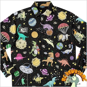 Puede incluir: Camisa negra con botones con un estampado colorido de dinosaurios con temática espacial. La camisa presenta varios dinosaurios con trajes de astronauta, planetas, estrellas y ovnis. El texto "BE RAWSOME" es visible en la esquina inferior derecha.