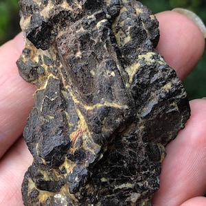 Puede incluir: Un cúmulo de cristales negros, brillantes y ligeramente iridiscentes con una superficie rugosa y texturizada. Los cristales están dispuestos en una forma irregular y dentada.