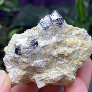Puede incluir: Un grupo de cristales negros y plateados incrustados en una roca gris clara. Los cristales tienen una forma geométrica afilada.