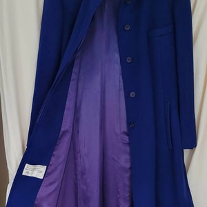 May include: A long, blue coat with a mandarin collar and a purple lining. The coat has a single button closure and two pockets. The label on the coat reads "JGHook".