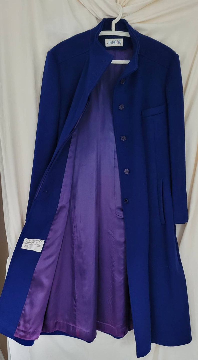 May include: A long, blue coat with a mandarin collar and a purple lining. The coat has a single button closure and two pockets. The label on the coat reads "JGHook".