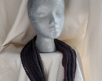 May include: A dark purple and black crocheted infinity scarf. The scarf is made of thick yarn and is long enough to be worn as a cowl.