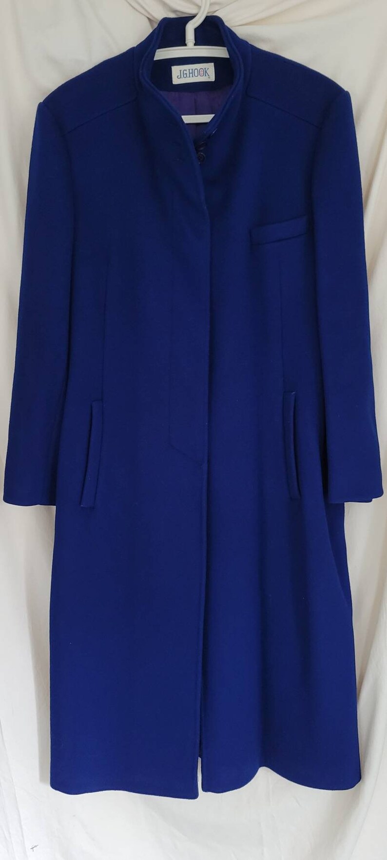 May include: A long, blue coat with a mandarin collar and a single button fastening. The coat has a label that reads "JGHOOK".