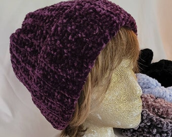 May include: A purple crocheted beanie hat with a textured, fuzzy surface. The hat is worn on a mannequin head with brown hair.