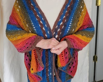 May include: A colourful crocheted shawl with a rainbow pattern in shades of red, orange, yellow, green, blue, and brown. The shawl is made with a lacy stitch and has a fringed edge.
