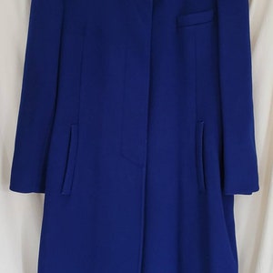 May include: A long, royal blue coat with a mandarin collar and a single button fastening. The coat has a small pocket on the left side and two side pockets. The label on the coat reads "JG HOOK."