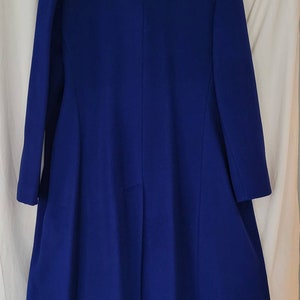 May include: A long, royal blue coat with a simple, elegant design. The coat has a high collar and long sleeves. The fabric is smooth and appears to be wool.