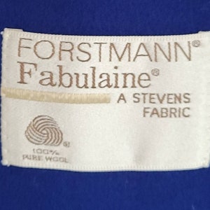 May include: A white fabric label with brown text that reads "FORSTMANN&reg; Fabulaine&reg; A STEVENS FABRIC 100% PURE WOOL". The label is attached to a royal blue fabric.