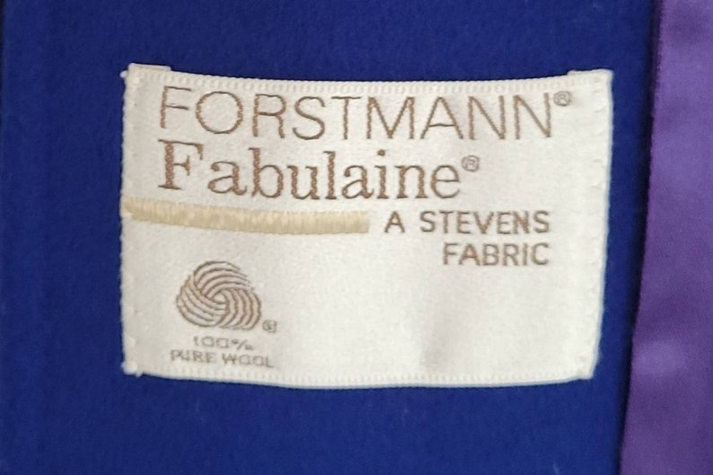 May include: A white fabric label with brown text that reads "FORSTMANN&reg; Fabulaine&reg; A STEVENS FABRIC 100% PURE WOOL". The label is attached to a royal blue fabric.