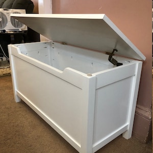 May include: White wooden storage chest with a hinged lid open. The chest has a simple design with a rectangular shape and a smooth finish.
