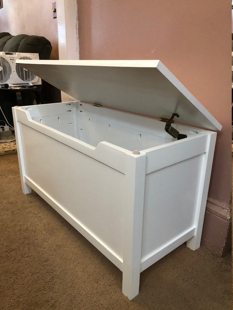 May include: White wooden storage chest with a hinged lid open. The chest has a simple design with a rectangular shape and a smooth finish.