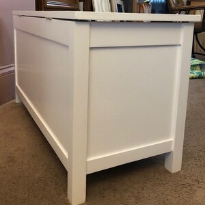 May include: White wooden toy chest with a hinged lid. The chest has a simple design with a raised panel on the front.