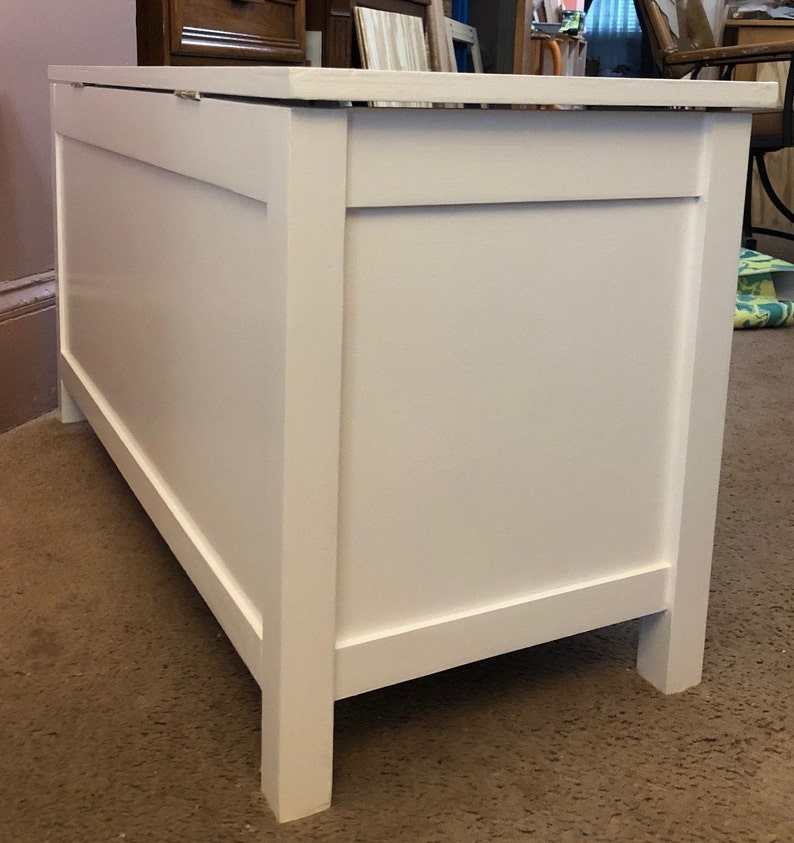 May include: White wooden toy chest with a hinged lid. The chest has a simple design with a raised panel on the front.