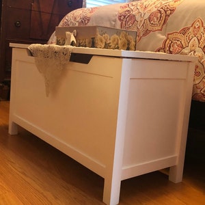 May include: White wooden storage chest with a decorative lace doily on top. The chest has a hinged lid and a simple design.