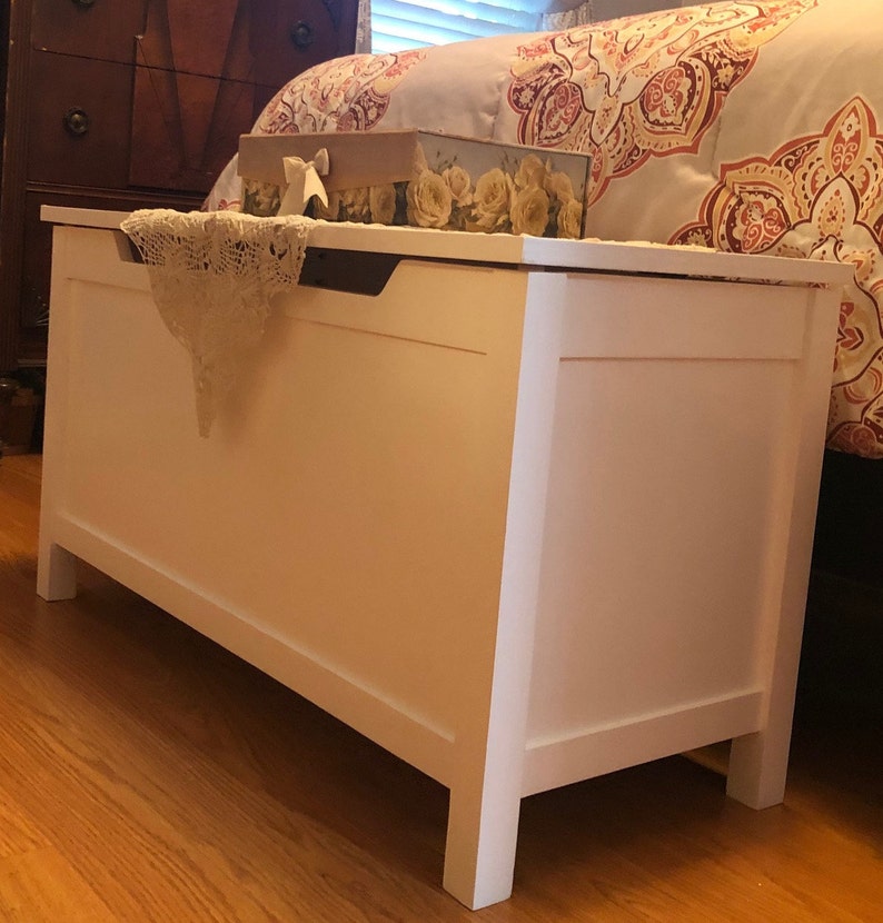 May include: White wooden storage chest with a decorative lace doily on top. The chest has a hinged lid and a simple design.