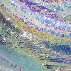 May include: Close-up of iridescent fabric with a scaly texture. The fabric is made of sequins in shades of blue, purple, and green.
