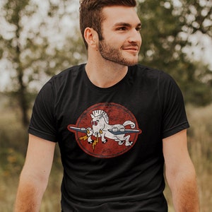 May include: A black t-shirt with a vintage-style graphic of a white unicorn riding a plane with a lightning bolt. The graphic is on a red circle with a white outline.