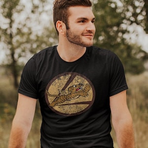 May include: A black t-shirt with a vintage-style graphic of a tiger flying in a circle. The graphic is in shades of brown and yellow.