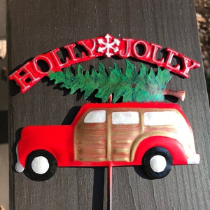 May include: Red metal Christmas decoration featuring a vintage car with a Christmas tree on top. The car has a wooden panel design and the words "HOLLY JOLLY" are above the car.