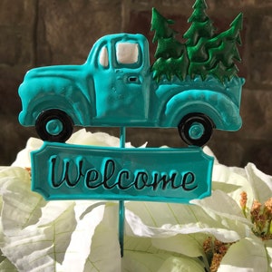 May include: A turquoise blue metal truck carrying a small green Christmas tree with a sign that says "Welcome".