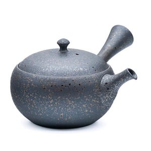 Puede incluir: Una tetera de cerámica gris con un acabado moteado y un diseño de pico único. La tetera tiene una tapa con un pequeño pomo en la parte superior.