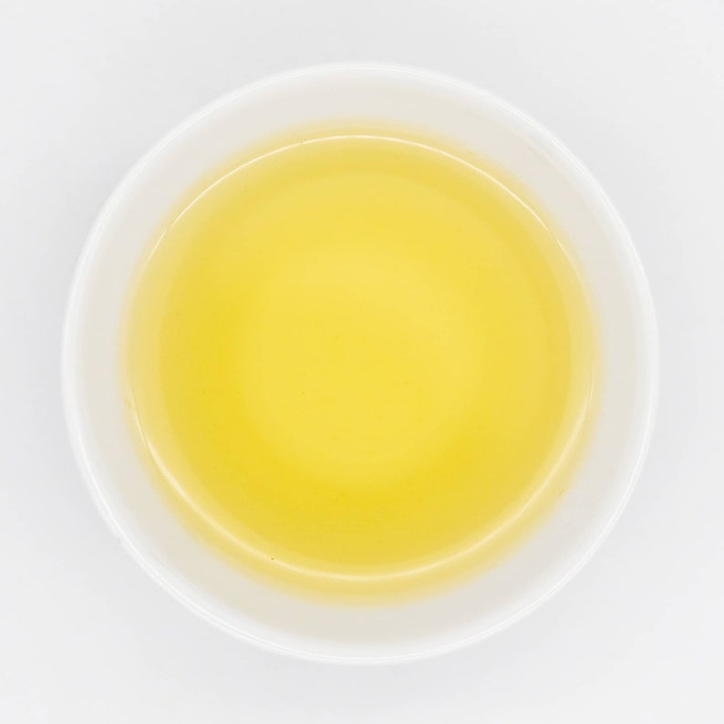 Puede incluir: Vista superior de un cuenco de cer&aacute;mica blanca lleno de un l&iacute;quido amarillo dorado. El cuenco tiene una forma simple y redondeada y se encuentra sobre un fondo blanco liso. El l&iacute;quido parece suave y transparente.