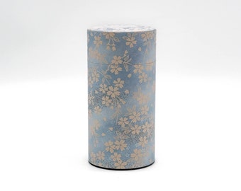 May include: A light blue cylindrical container with a white floral pattern. The container is made of paper and has a smooth surface.