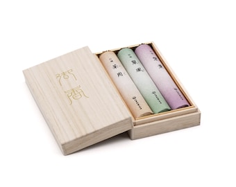 May include: A wooden box with a sliding lid, containing three rolls of incense. The box is labeled with the Japanese characters "香房". The incense rolls are wrapped in paper and have different colors and scents.