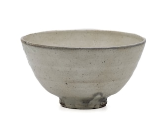 May include: A handmade, off-white ceramic bowl with a wide, angled design. The bowl has a textured surface with dark speckles and a dark rim. The base is a darker shade of brown. This bowl is perfect for serving soups, salads, or other dishes.