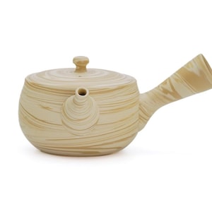 May include: A beige ceramic teapot with a matching lid and a side handle. The teapot has a rounded body and a spout. The surface has a swirled pattern in a lighter beige color. The teapot is designed for brewing tea.