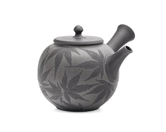 Pode incluir: Uma chaleira de cerâmica cinza com um design de folhas. A chaleira tem uma tampa e um bico.